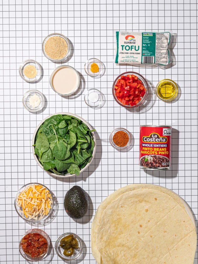 flat lay of ingredients for tofu breakfast burritos: spinach, red pepper, taco seasoning, tofu, tortillas, pinto beans