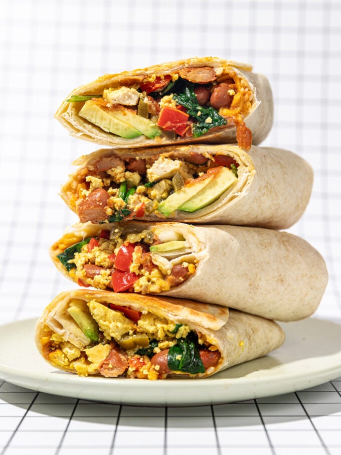 stack of 4 tofu breakfast burritos with avocado, spinach and red pepper on a white plate