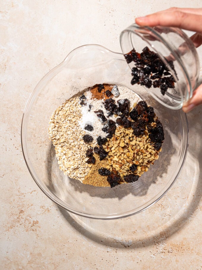 hand adding diced prunes to mixing bowl with cookie ingredients