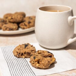2 prune cookies on a napkin, beside a mug of coffee and plate of cookies