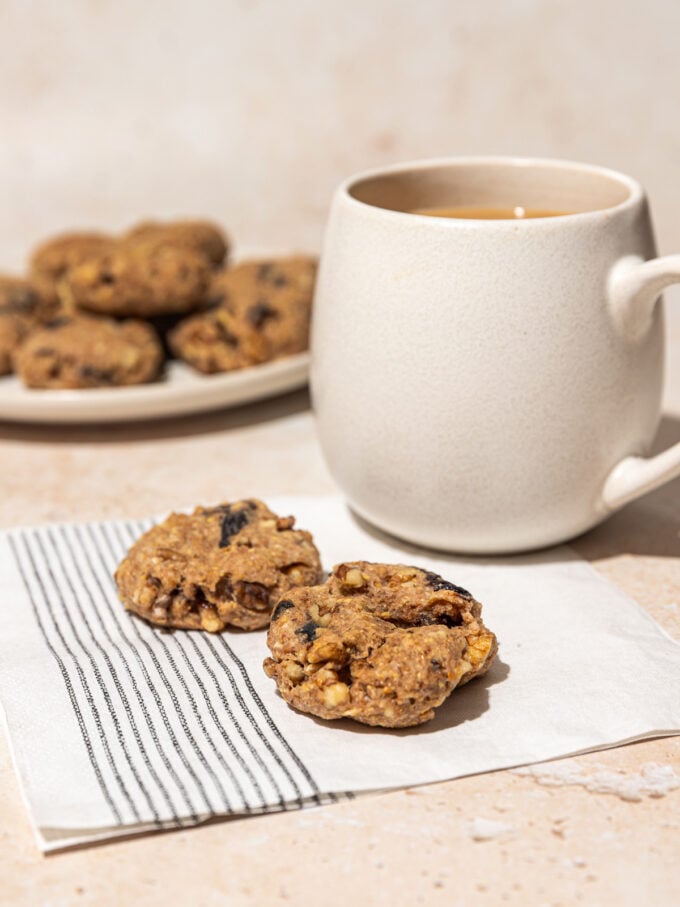 2 prune cookies on a napkin, beside a mug of coffee and plate of cookies
