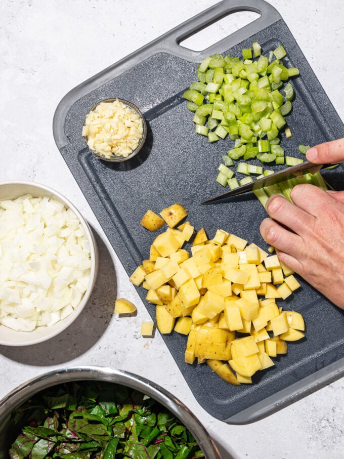 hand dicing celery on black cutting board with diced potatoes