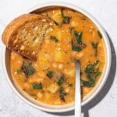 white bean stew in a white bowl with a spoon and slice of toast dunked in