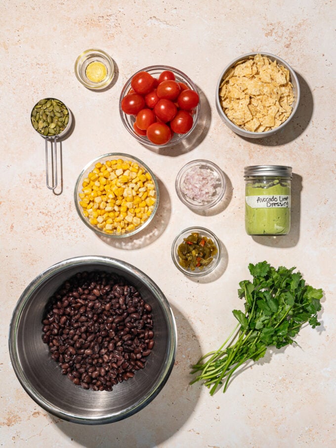 black bean salad ingredients in bowls: black beans, corn, cherry tomatoes, shallot, crushed tortilla chips