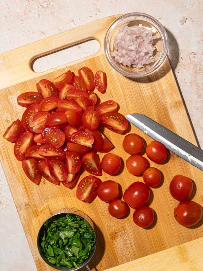 wooden cutting board with sliced cherry tomatoes, minced cilantro and shallot