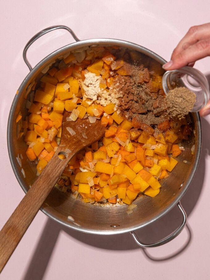 hand adding spices to pot of cooked butternut squash