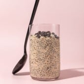 glass filled with cookie dough overnight oats with a black spoon leaned up against it, on a pink background