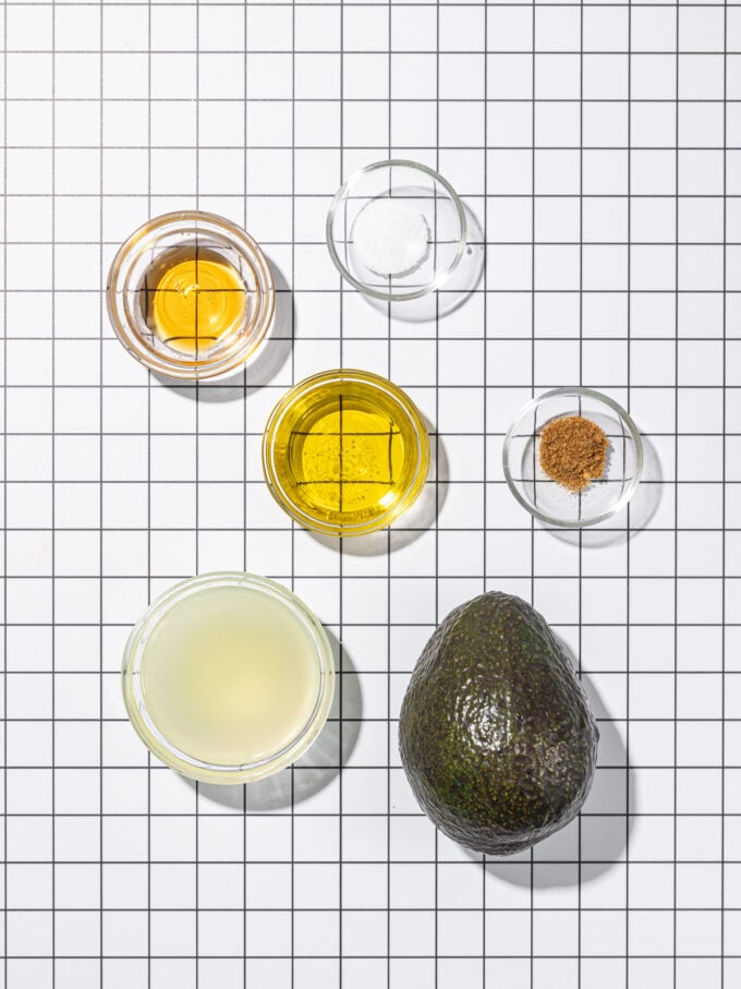avocado arranged beside small bowls of ingredients: oil, lime juice, cumin, salt, maple syrup