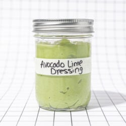 Glass jar of avocado lime dressing, labelled, on a black and white grid background