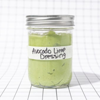 Glass jar of avocado lime dressing, labelled, on a black and white grid background