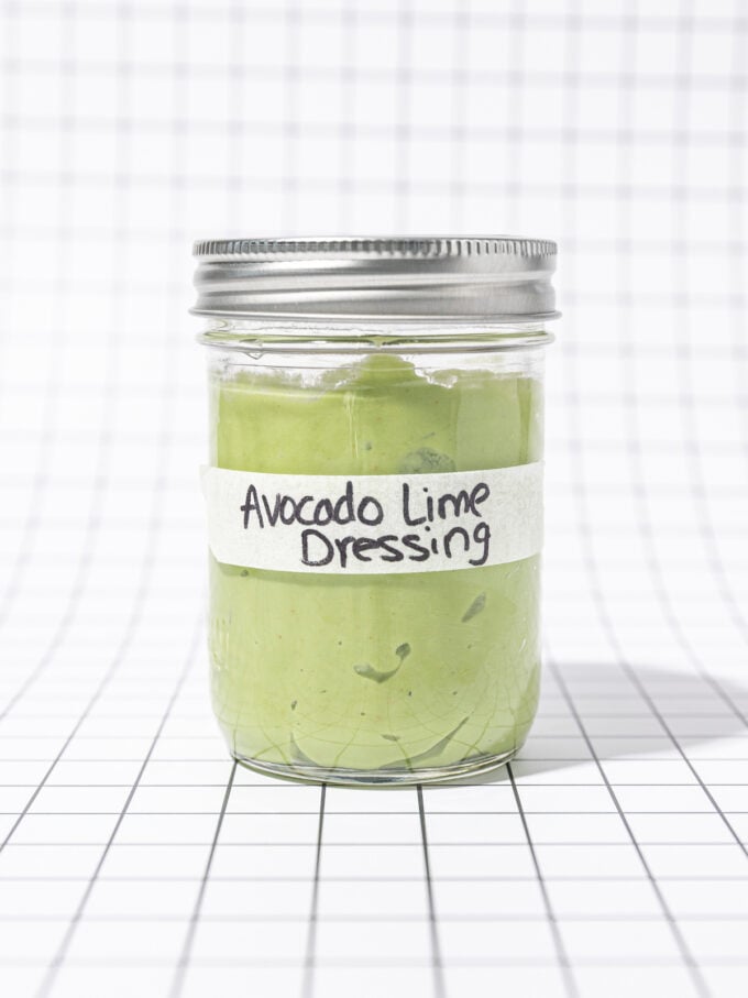 Glass jar of avocado lime dressing, labelled, on a black and white grid background