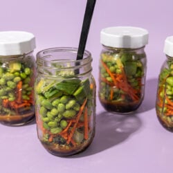 4 glass jars filled with edamame salad on a purple background
