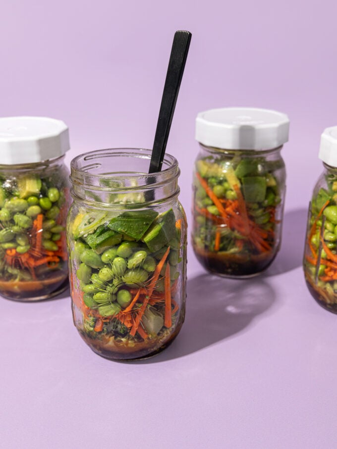 4 glass jars filled with edamame salad on a purple background