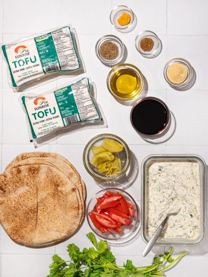 tofu shawarma ingredients: 2 packages of tofu, whole wheat pita, tomatoes, tamari, spices in bowls and tzatziki