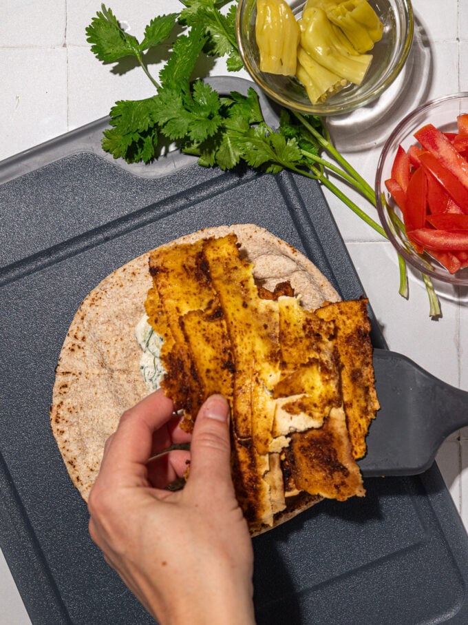 hand placing tofu shawarma on pita bread on black cutting board