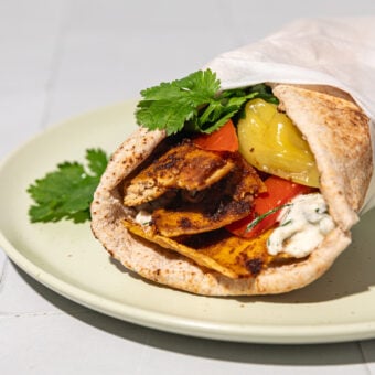 shaved tofu shawarma wrapped in pita with cilantro, tzatiki and tomato on beige plate