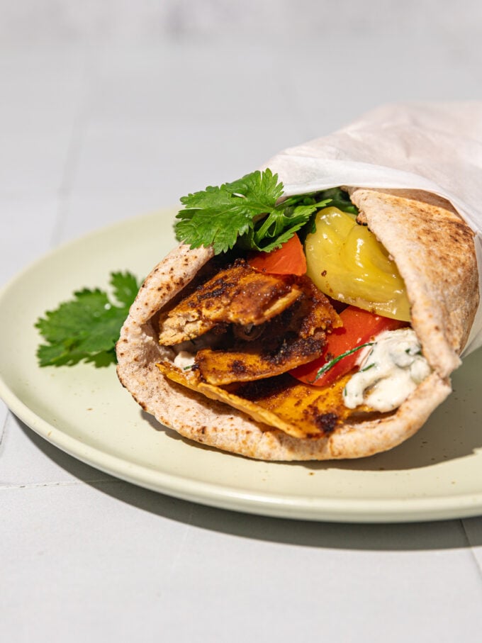 shaved tofu shawarma wrapped in pita with cilantro, tzatiki and tomato on beige plate
